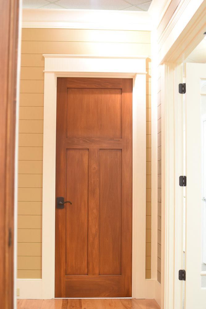 Wooden door with three panels, surrounded by white trim and set in a tan wall.