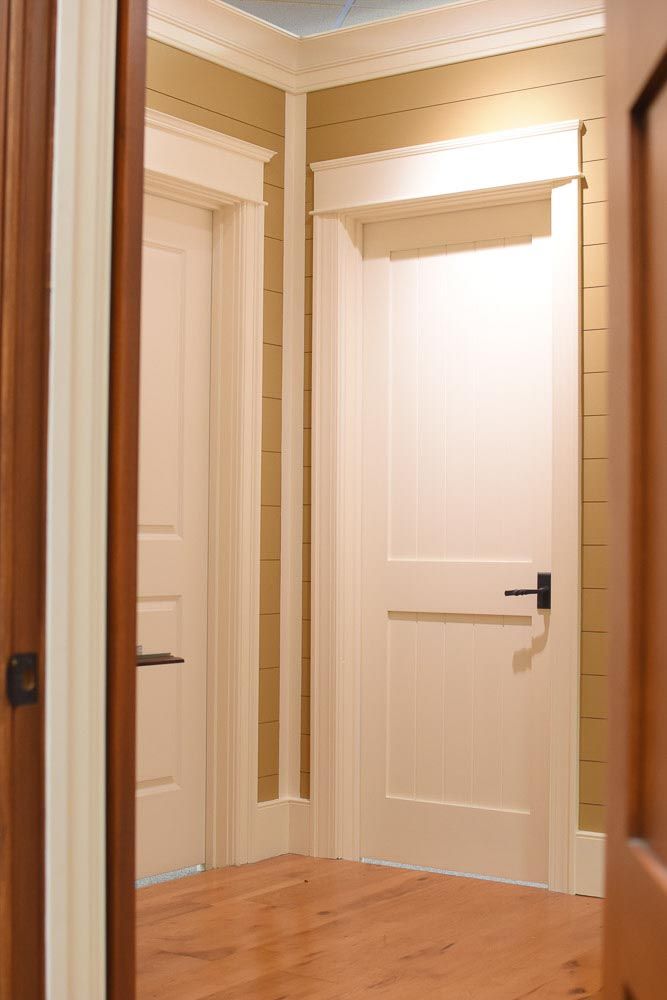 Two interior doors, one open. White doors with dark handles in a hallway with light-colored walls and wood floor.