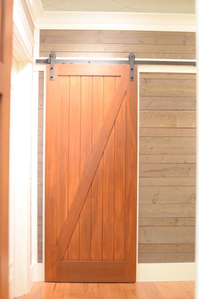 Wooden barn door with diagonal support beam on a track, against a wood-paneled wall.