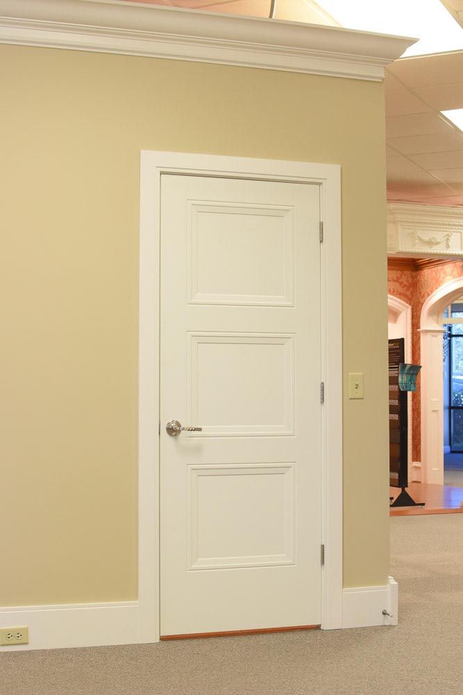 White paneled door in a tan walled room, with white trim and a silver door handle.