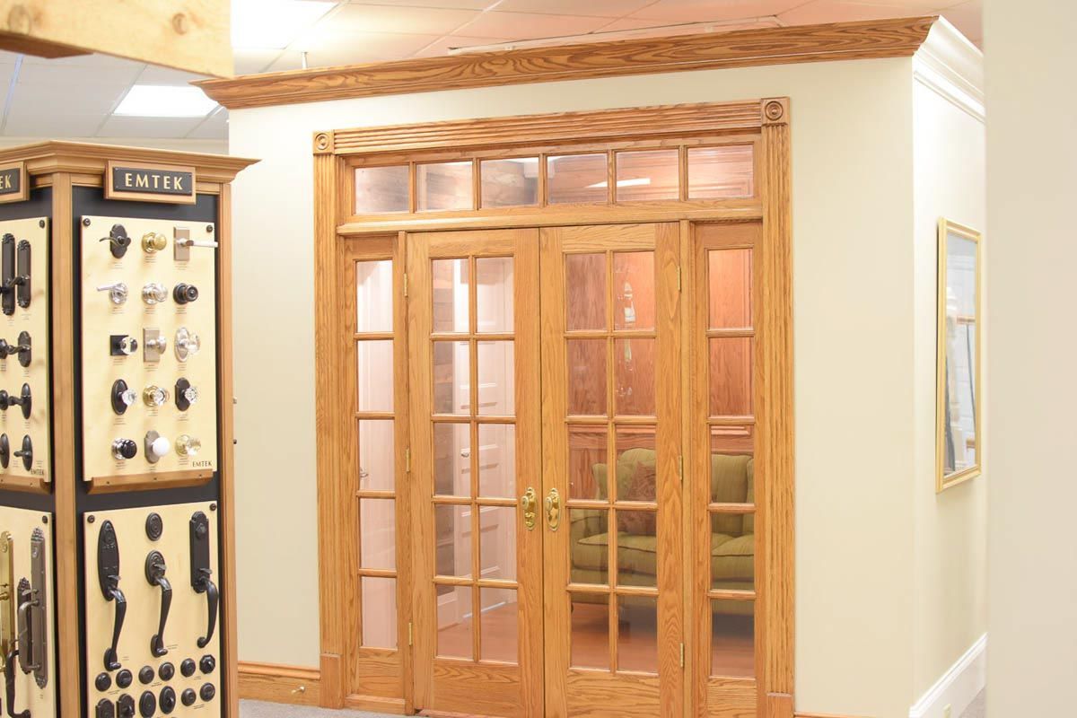 Wooden double doors with glass panes, framed by light-colored wood, and adjacent display of doorknobs.