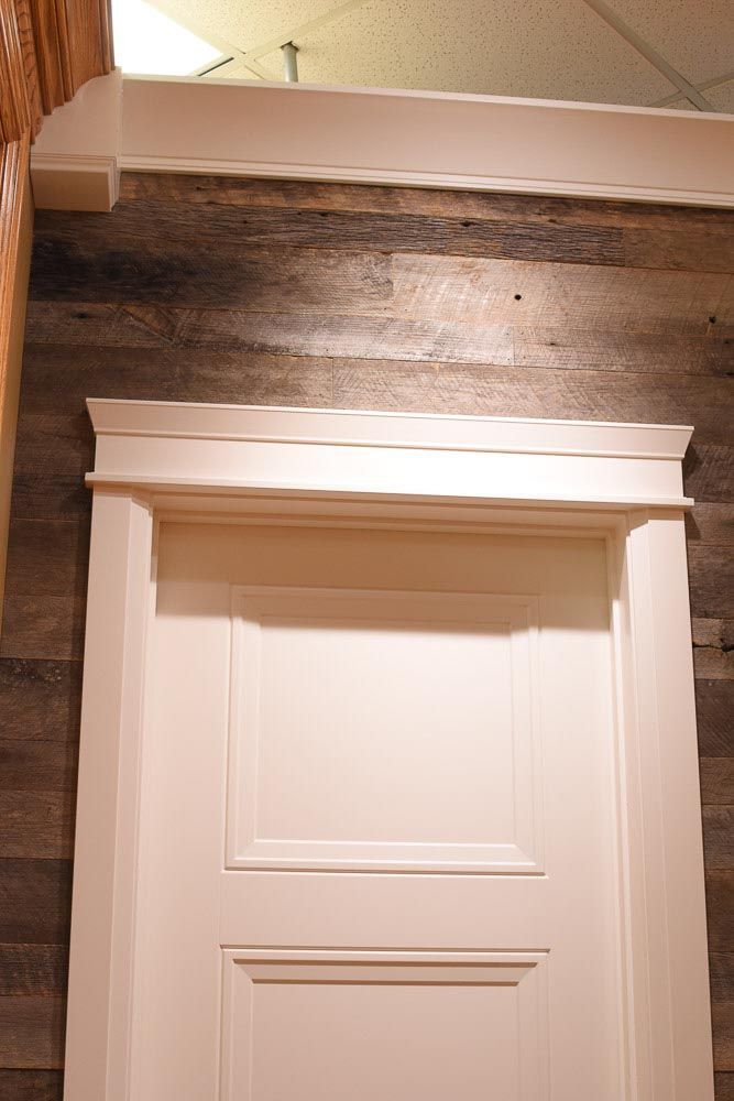 White door with decorative molding against wood-paneled wall, crown molding above.