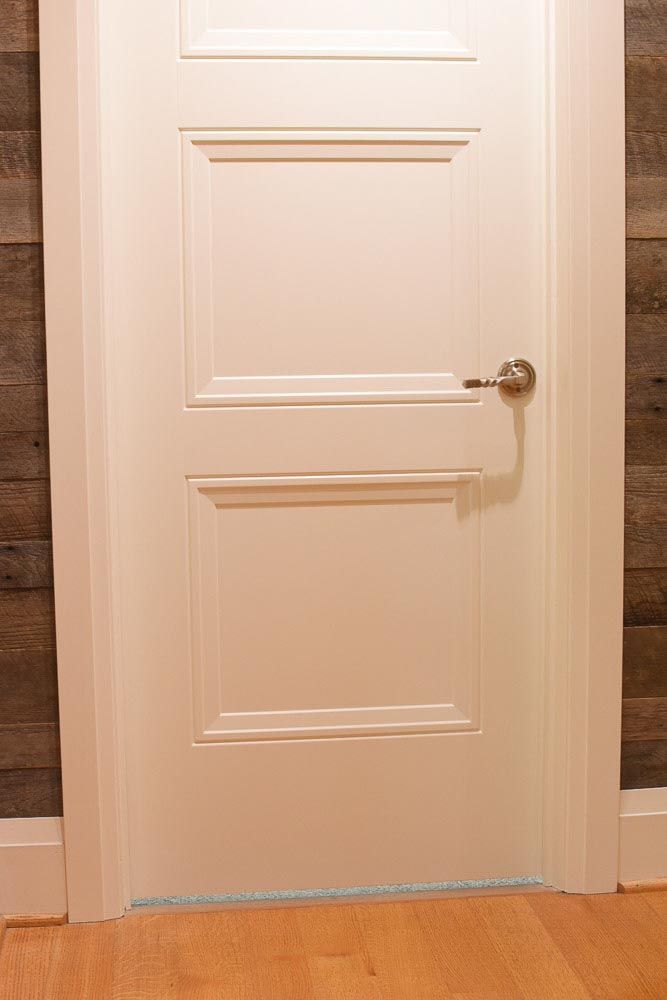White door with two recessed panels and silver handle, set in white frame against wood-paneled wall.