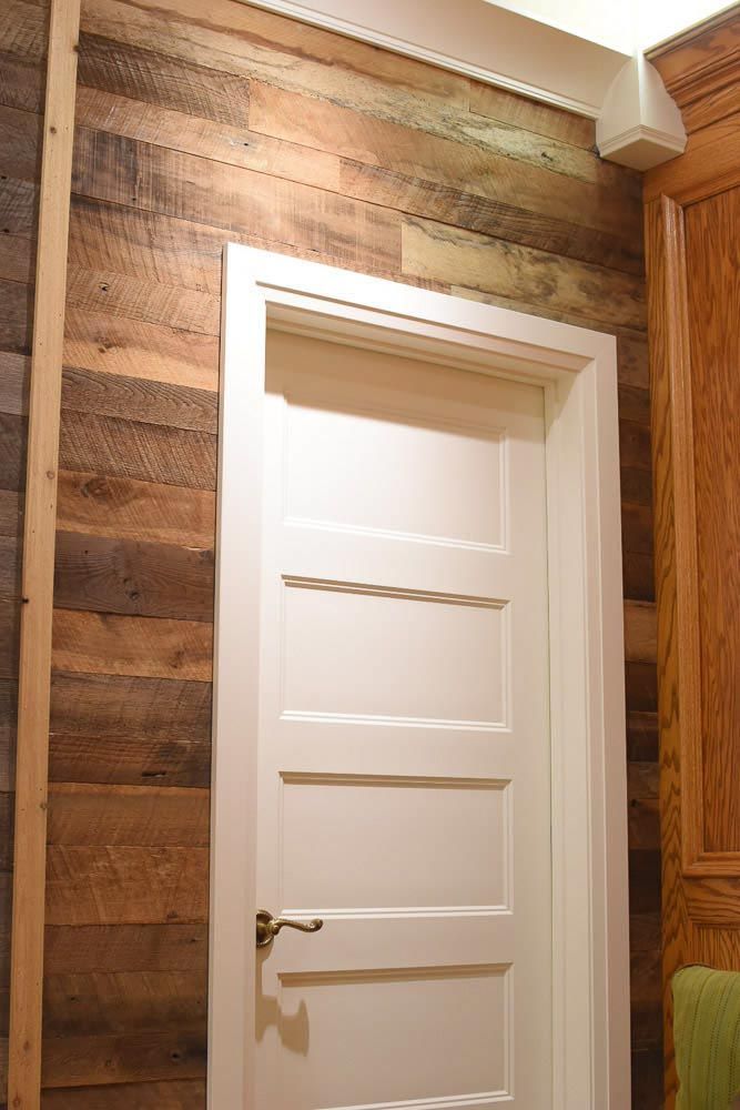 White door in wooden plank wall, framed by white trim and a speaker.
