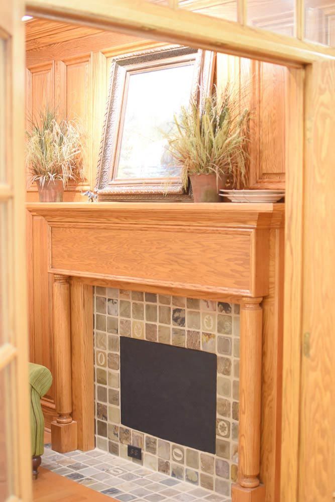Wooden fireplace with tile surround, framed art, and potted plants.
