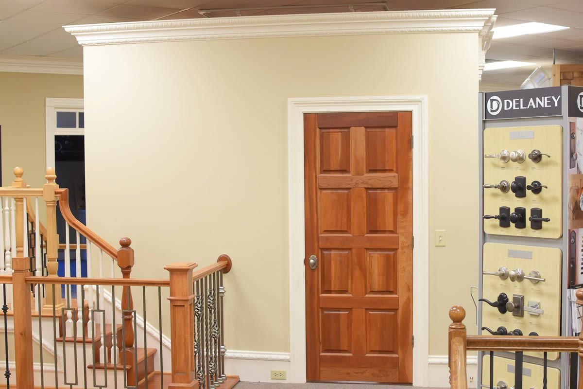 Wooden door in a beige room with crown molding, staircase on the left, hardware display on the right.