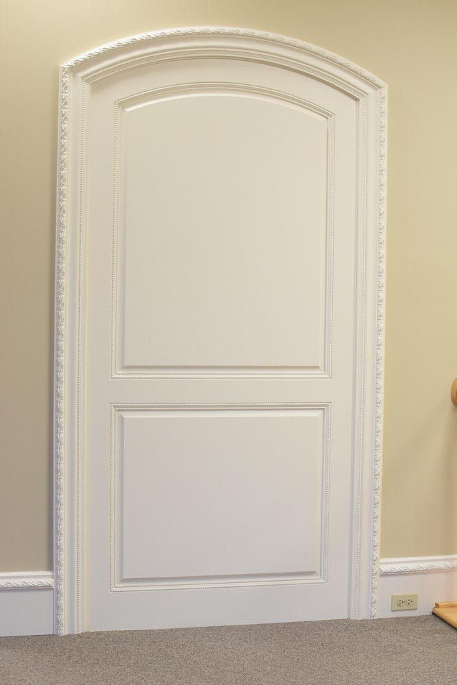 White interior door with arched top and decorative trim, set in a light beige wall.