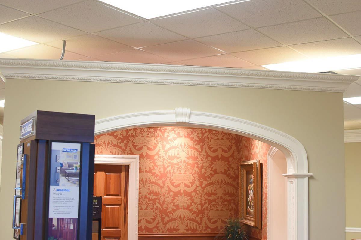Archway with crown molding and patterned wallpaper, leading to a door and painting.