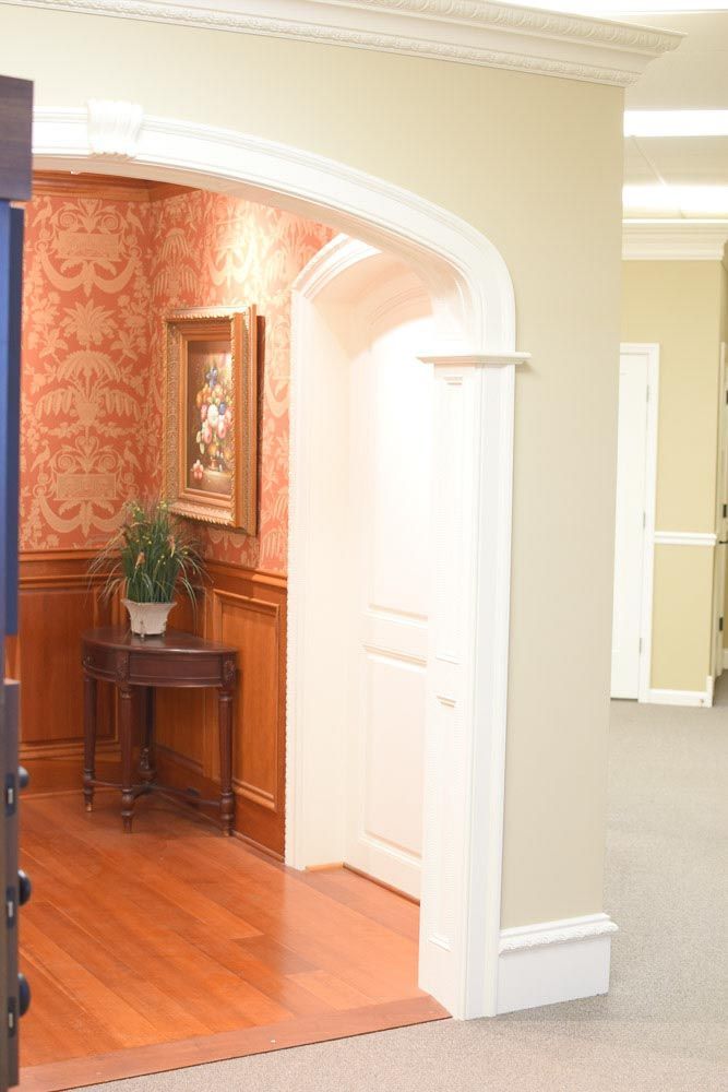 Interior hallway with an arched doorway leading to a room with wood paneling, red patterned wallpaper, and a painting.