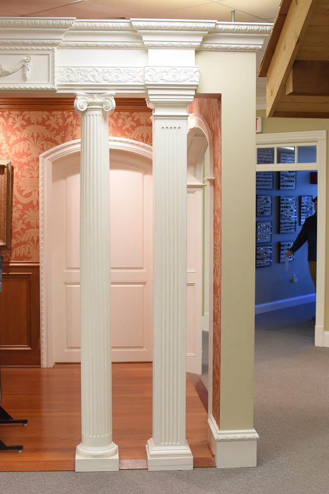 Two white columns with decorative molding, leading to a door, in a room with wood flooring.