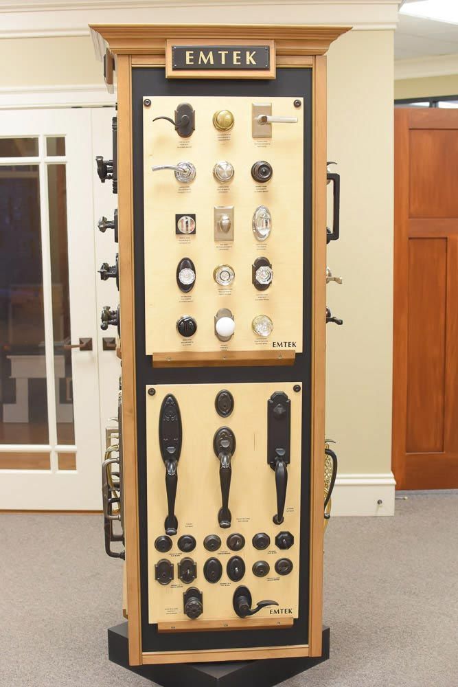 Display of Emtek door hardware: knobs, levers, and handles in a showroom. Beige and black, with wooden display.