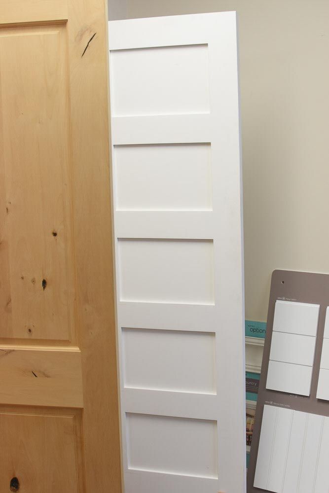 White six-panel interior door leaning against a wall, next to a wood door.
