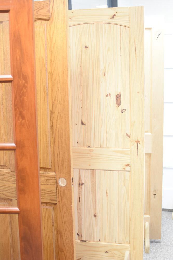 Several wooden doors, varying in color and design, stand close together in a showroom.