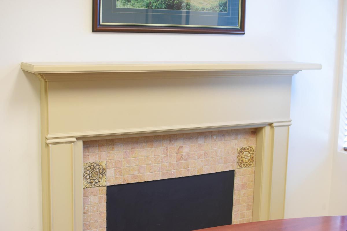 Cream-colored fireplace with a black interior, mosaic tile surround, and a framed picture above.