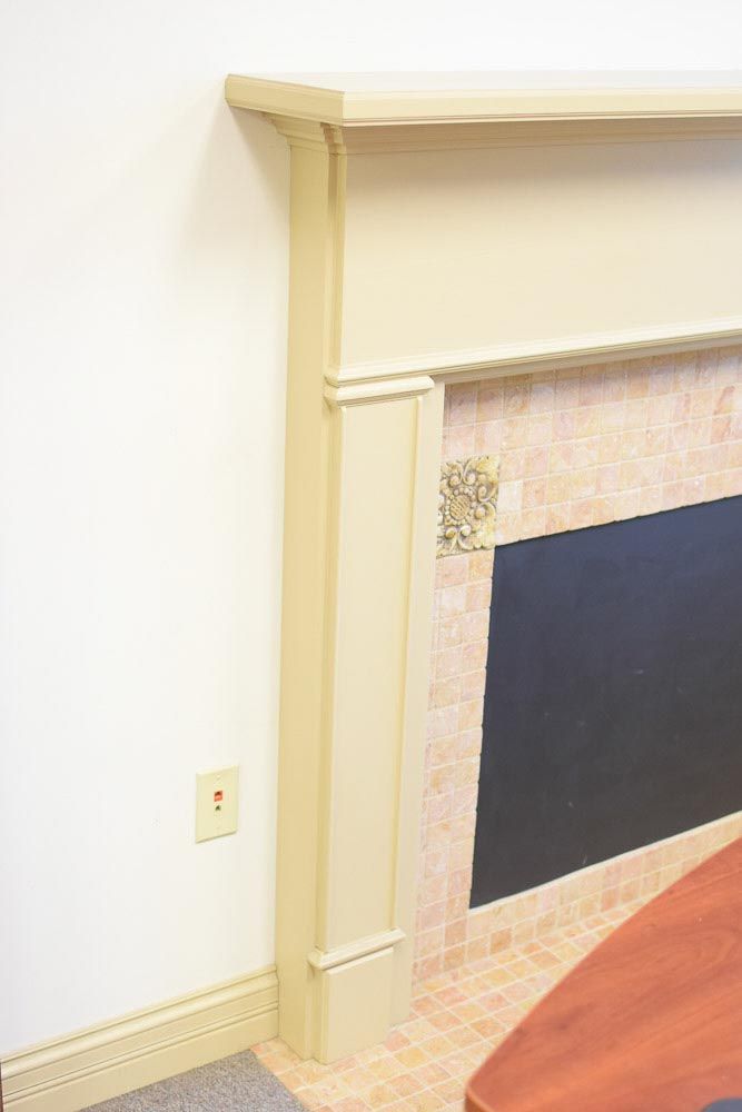 Cream-colored fireplace mantle on a white wall. The fireplace has a tile surround and a dark inset.