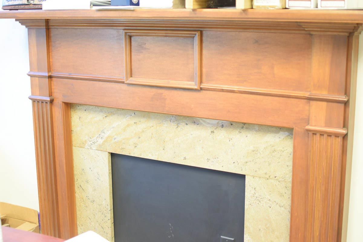 Wooden fireplace mantel with a light-colored stone surround and a black fireplace insert.