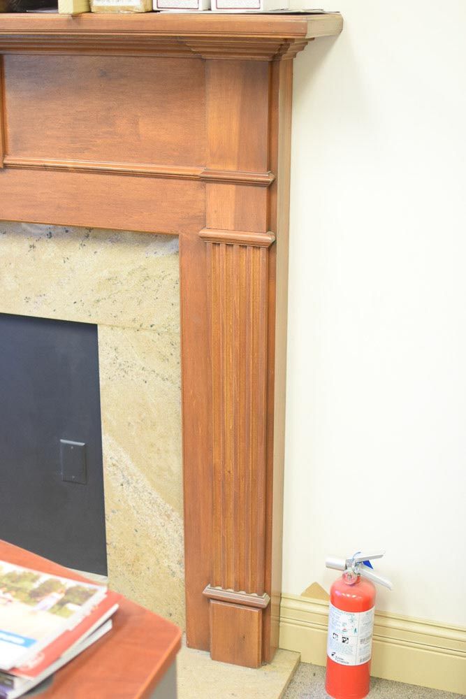 Wooden fireplace with decorative details and a red fire extinguisher nearby.