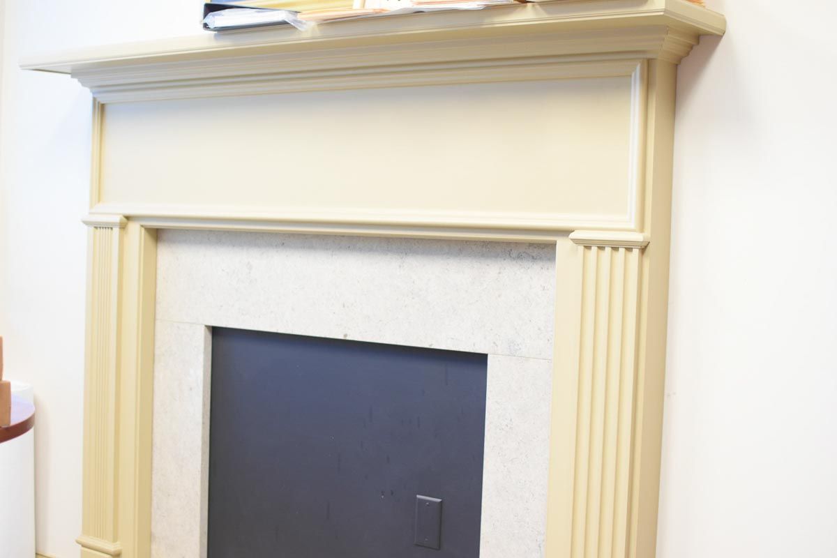 Cream-colored fireplace with a black insert and light-colored stone surround. A shelf is above.