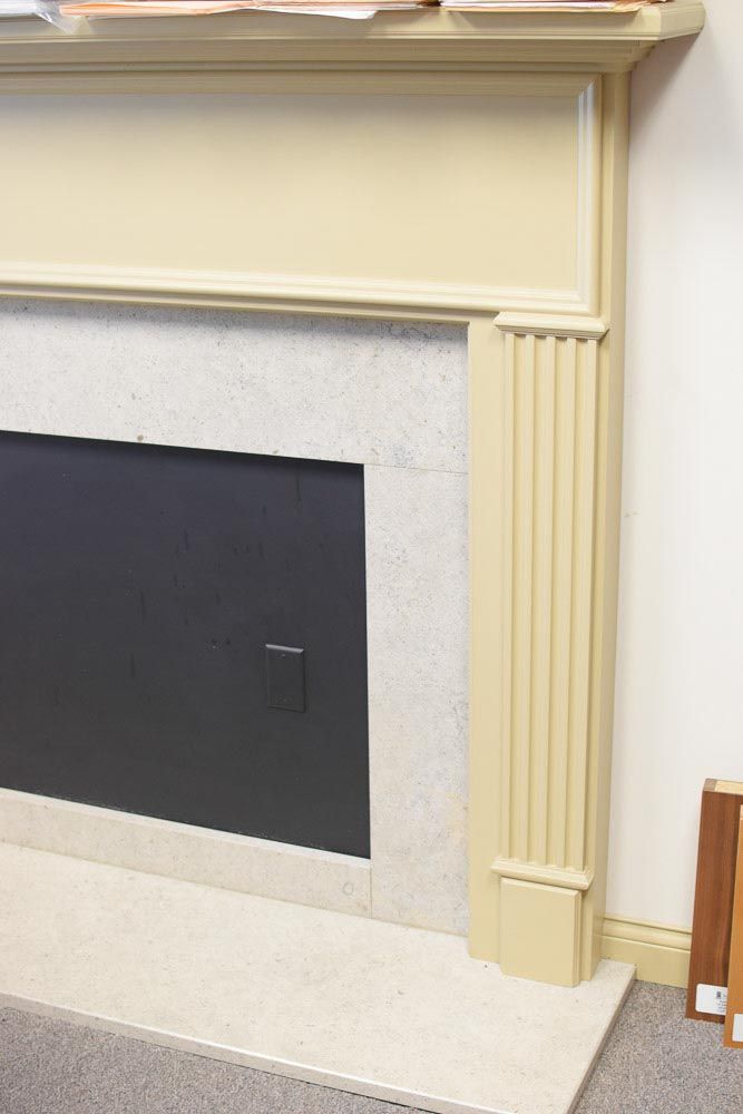 Fireplace with a cream-colored mantel, fluted column detail, and a black firebox set against a light-colored stone surround.