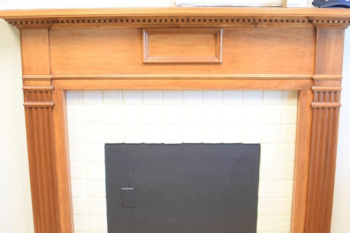 Wooden fireplace mantel with white tiled surround and black firebox door.