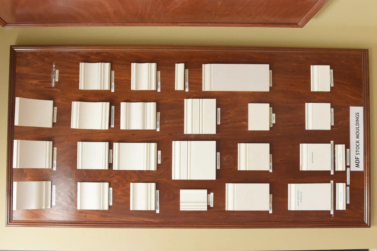 Wooden board displaying various white rectangular architectural trim samples.