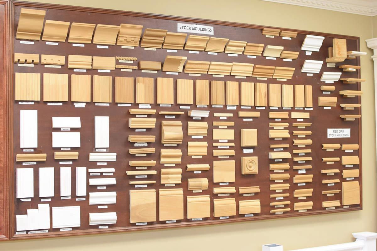 Display of various wood trim profiles, mounted on a large brown board for selection.