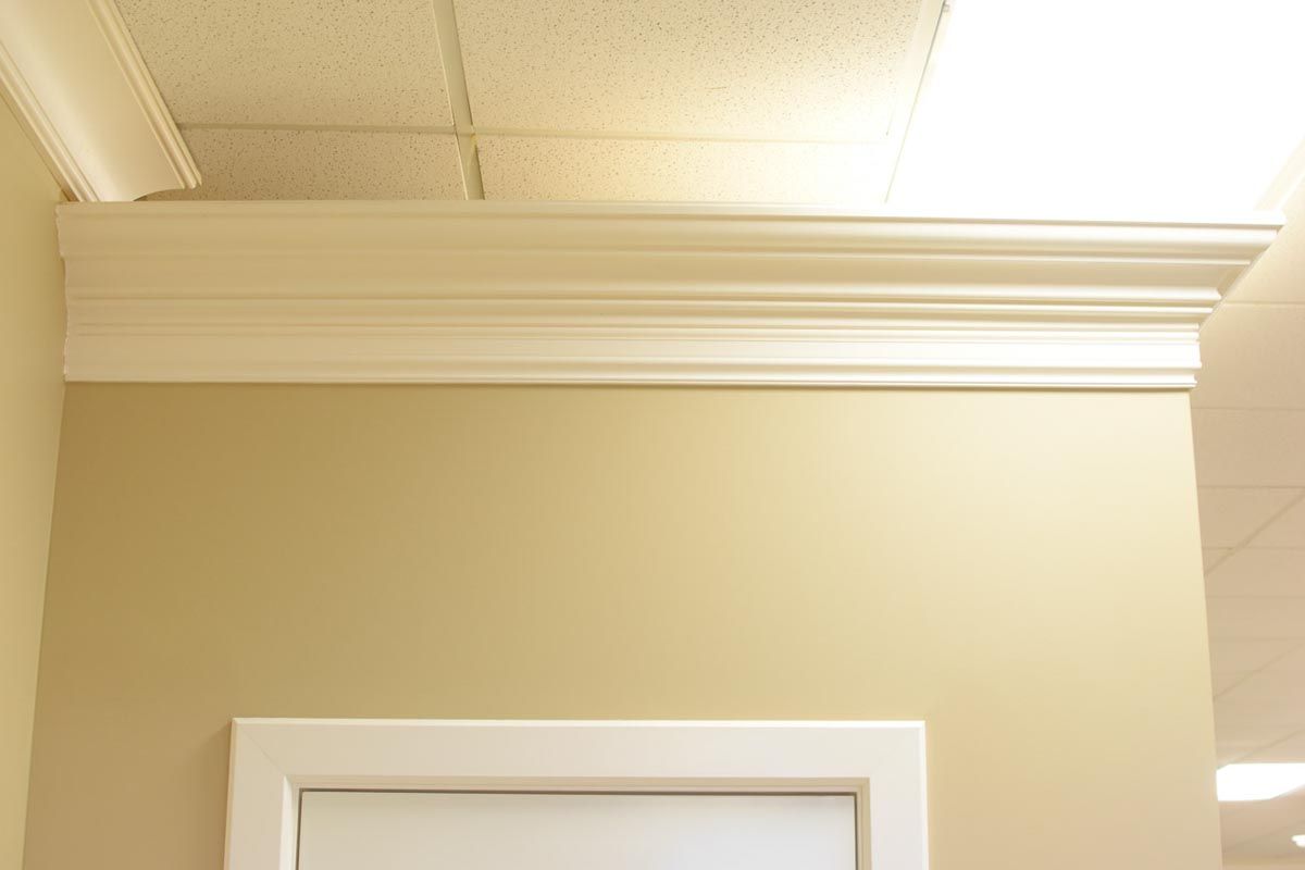 White crown molding atop a beige wall, above a white door frame.