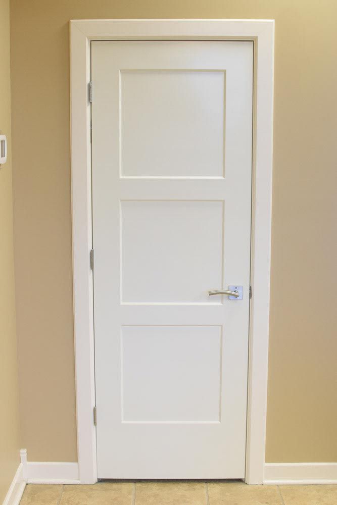 White three-panel door, silver handle, white trim, beige walls, and tan floor.