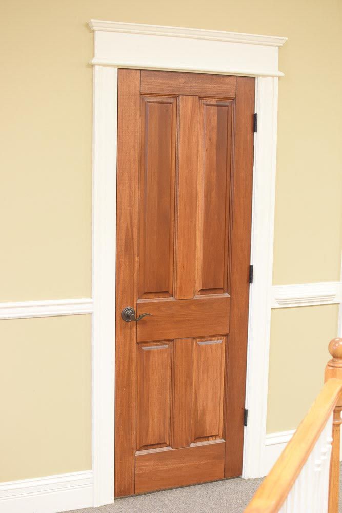 Wooden door with white trim, set in a yellow wall. Stair railing visible on the right.