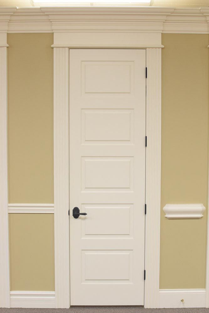 White, five-panel door with black hardware, surrounded by white trim and beige walls.