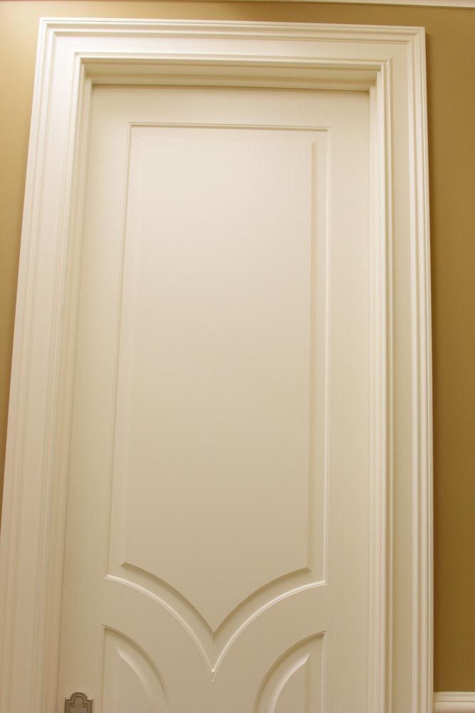 White paneled interior door with decorative molding, set in a tan-colored wall.