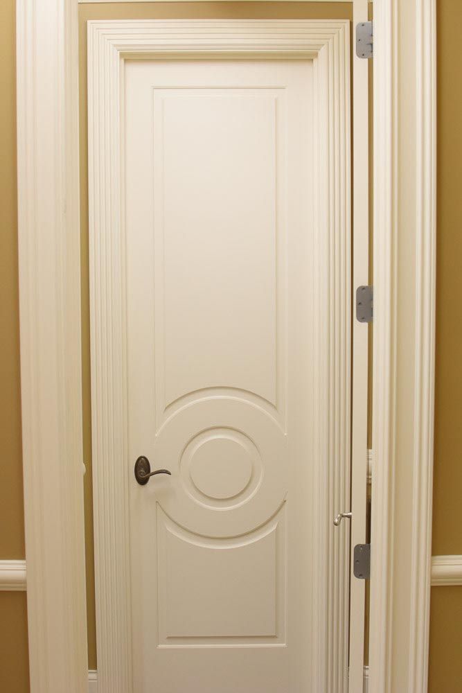 White interior door with circular design, partially open, within a doorway with molding, set against light yellow walls.