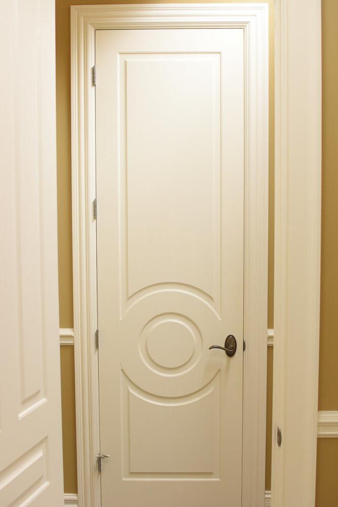 White paneled interior door with decorative circular design and bronze handle.