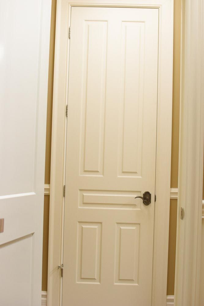 White paneled interior door with bronze hardware, framed by light-colored walls.