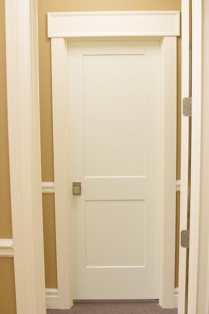 White door with a two-panel design, set in a white frame, against a tan wall.