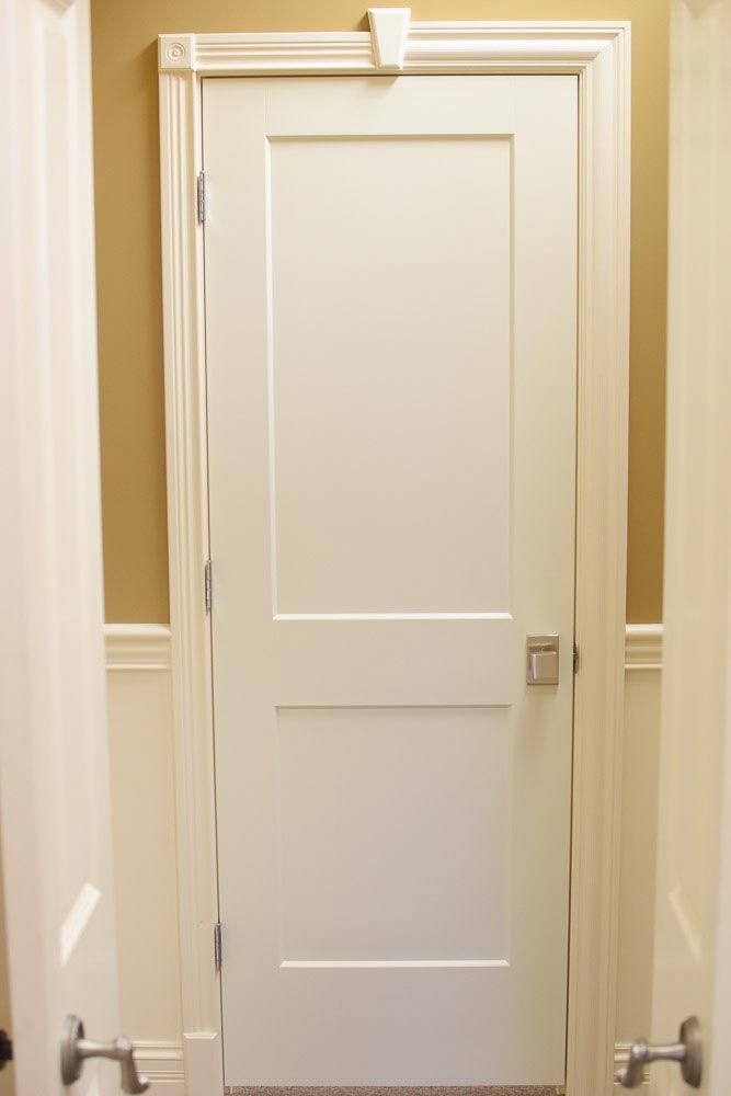 White door in a doorway, with molding and a door closer; light brown and white walls.