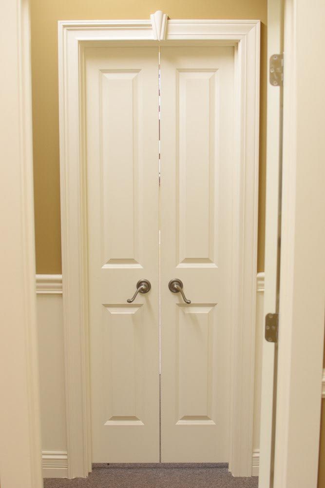 Double white interior doors with round silver handles, framed by white molding, in a beige hallway.