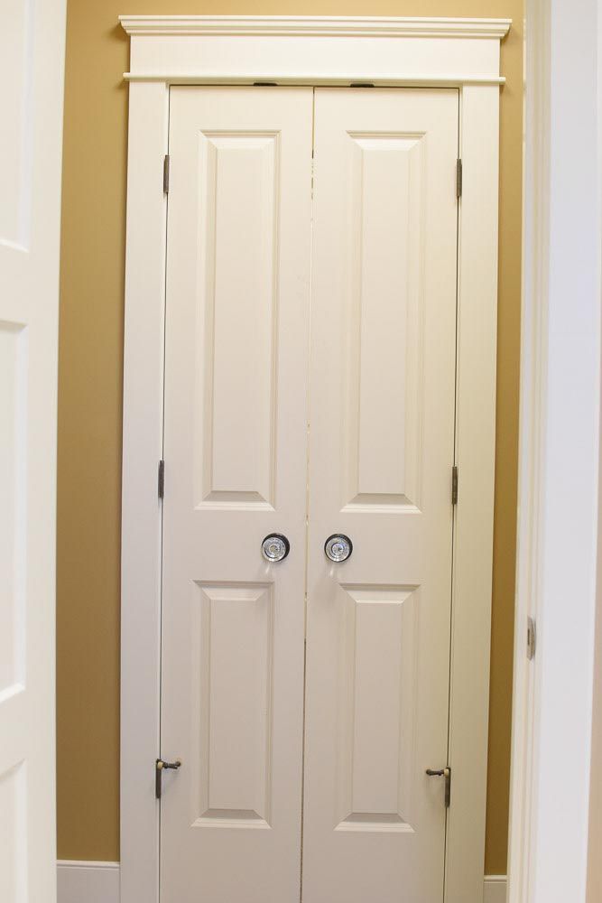 White bi-fold closet doors with decorative trim, set against a light beige wall and white trim.