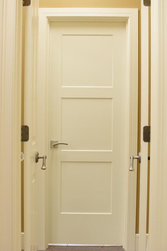 White 3-panel door with silver handle in a neutral-colored hallway.