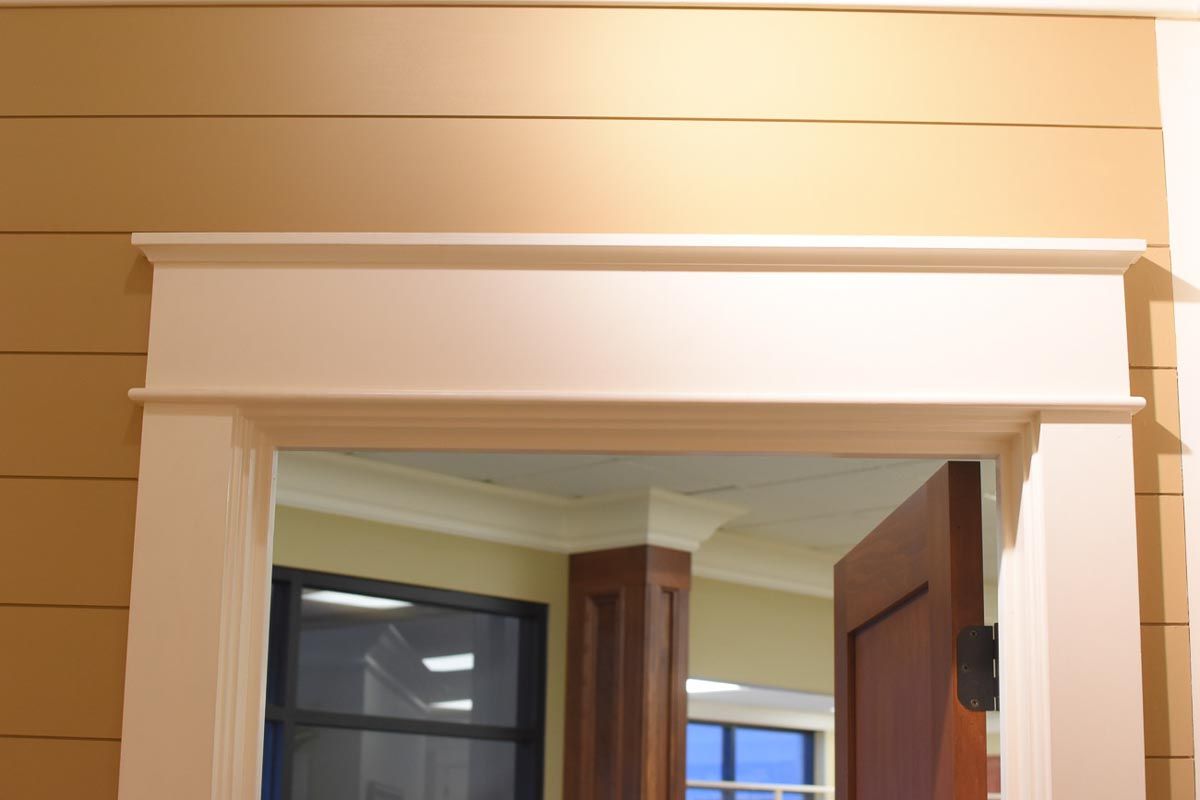 White door frame with detailed molding against tan horizontal siding. Interior view with partially open brown door.
