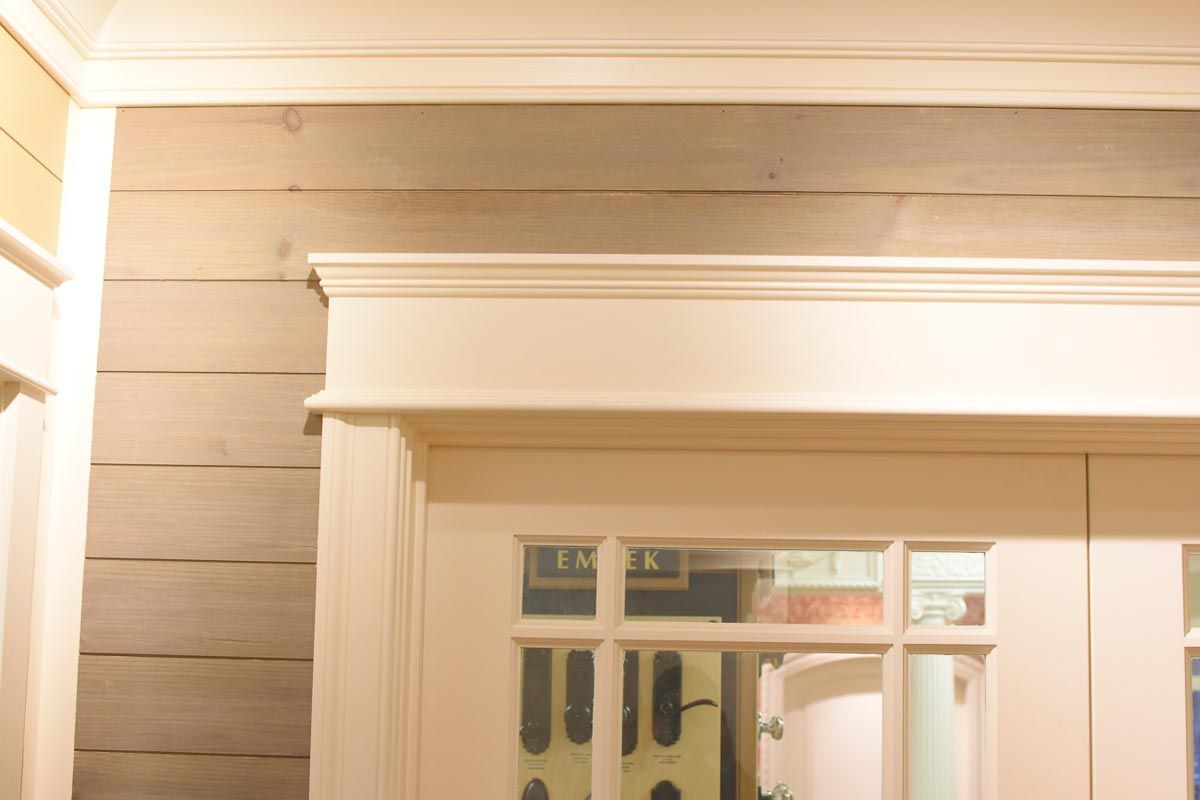 Corner of a room with white trim and grey horizontal wooden planks. Brightly lit with window reflection.