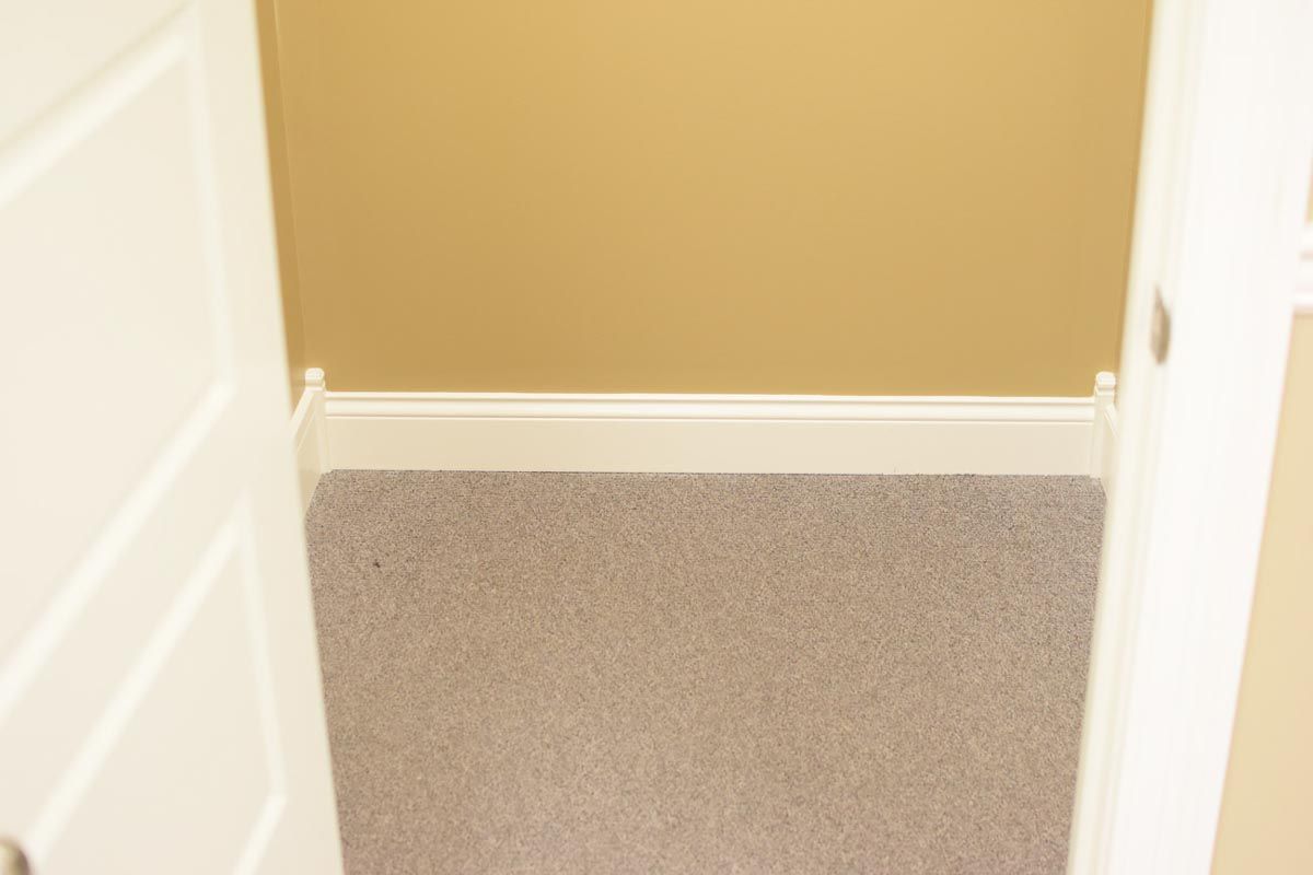 View from a closet with gray carpet and tan walls. White doors frame the opening.