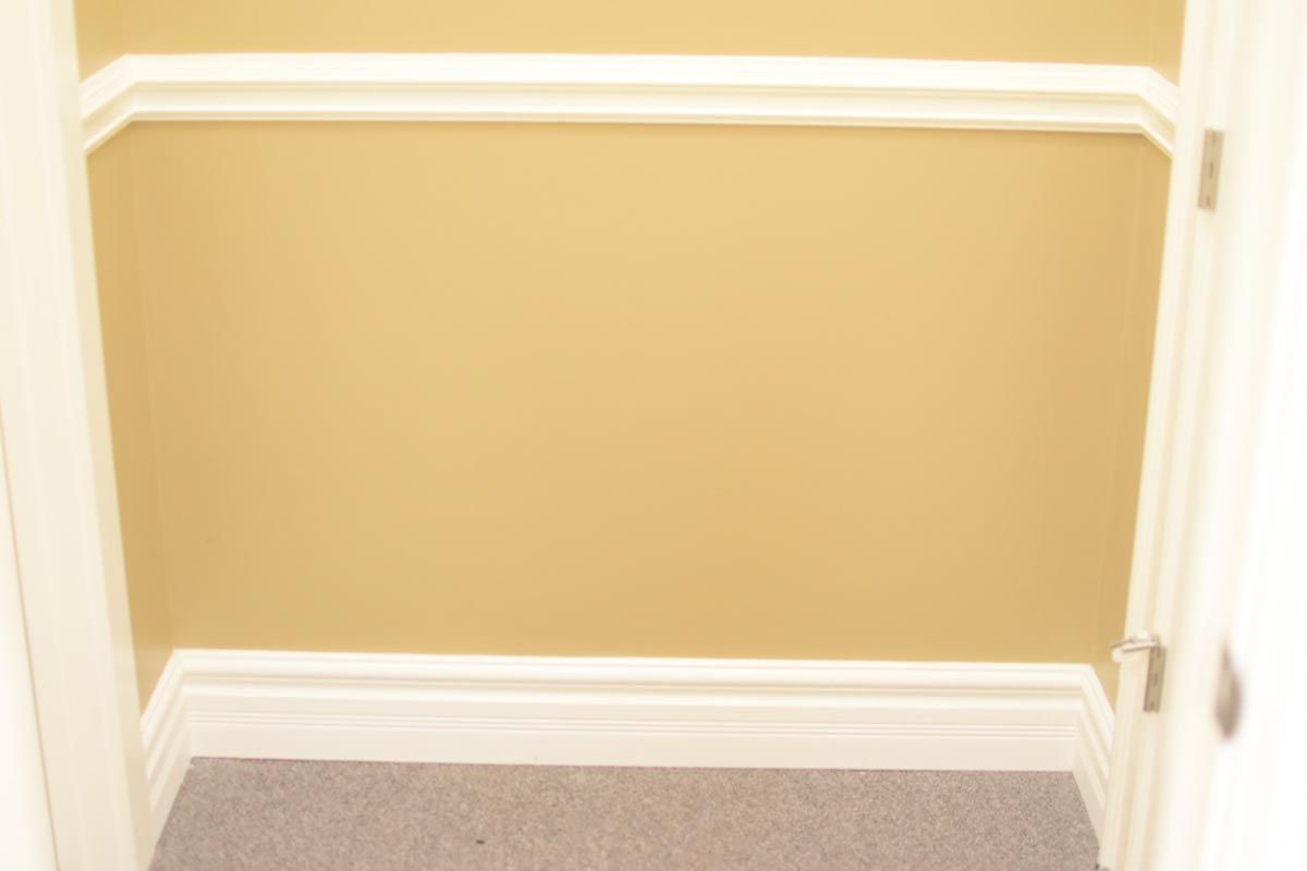 Empty closet interior, tan walls with white trim, gray carpeted floor.