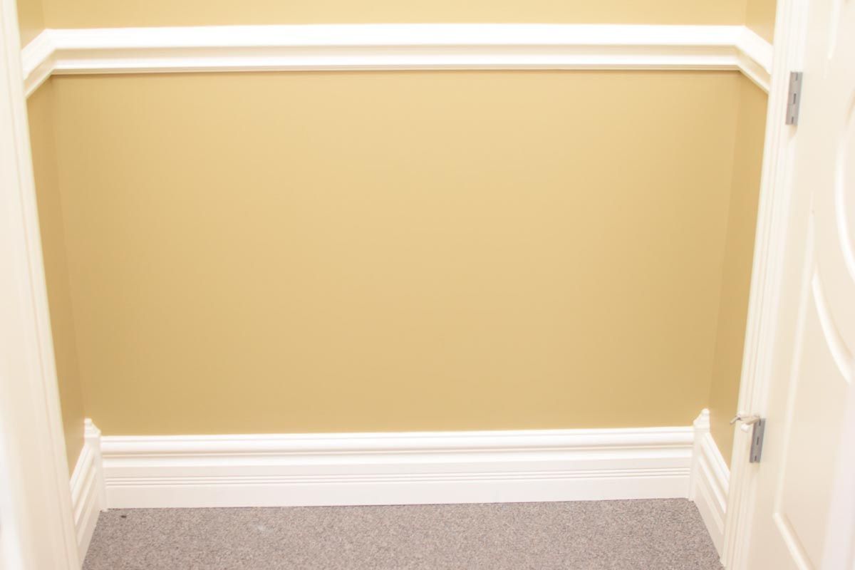 Tan wall with white molding, doorway opening onto gray carpet.