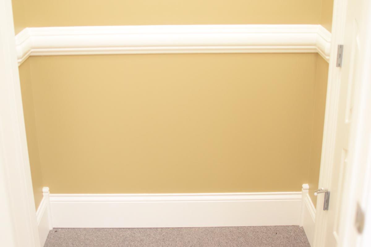 Beige walls and trim with a shelf, above a carpeted space.
