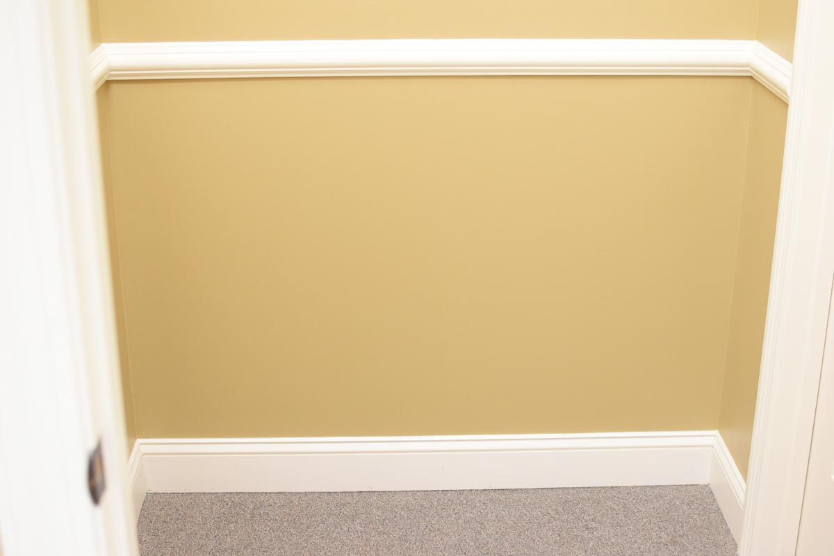 Empty closet with gold walls, white trim, and gray carpet.