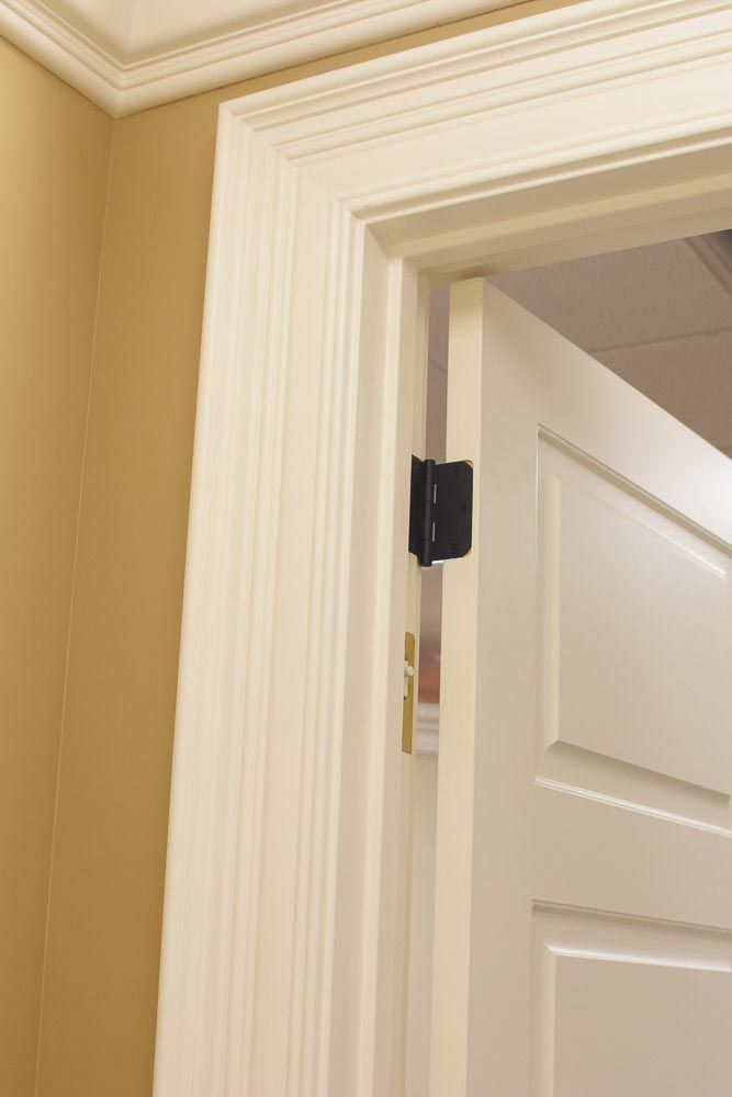 White door frame with open white door, black hinge, tan wall.