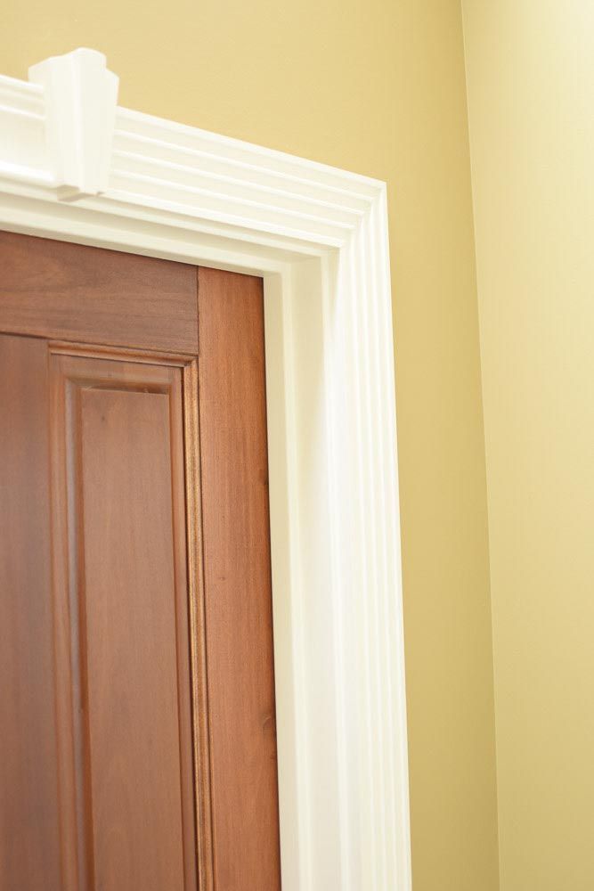 Close-up of a brown door and white door frame with detailed molding against a yellow wall.
