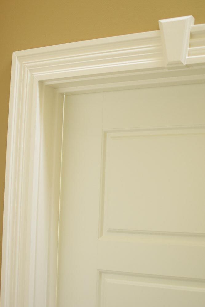 White door frame with molding, a white door, and a white, rectangular object attached to the top frame.