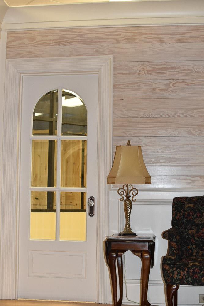 White door with arched glass panels, lamp on small table, and wood-paneled walls.